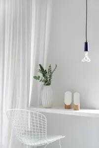 A minimalist home office with a white desk, white wire chair, green plant, and white hanging light.