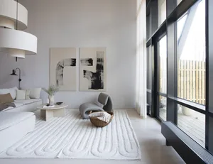 A modern minimalist living room with white walls, a grey lounge chair, and a white rug with an abstract design.