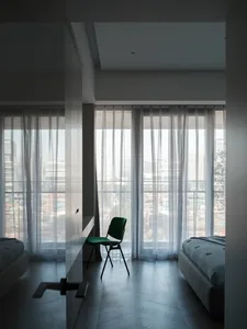 Minimalist bedroom featuring transparent fabric curtains and a green chair.