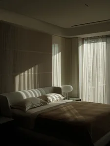 A minimalist bedroom with a textured accent wall, featuring a bed with white bedding and a modern table lamp.