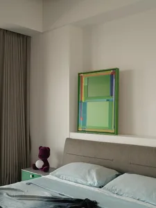 A modern bedroom featuring a bed with turquoise bedding, a green fabric headboard, and a green-framed abstract painting.