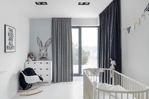 A minimalist bedroom featuring black and white furniture and decor with a white crib, rocking chair, and window with black cu
