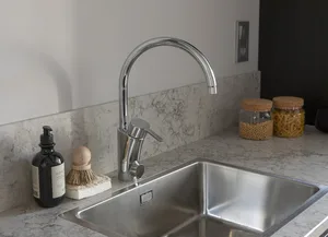 Modern kitchen featuring a stainless steel sink with a curved faucet, mounted on a marble countertop with jars of grains.