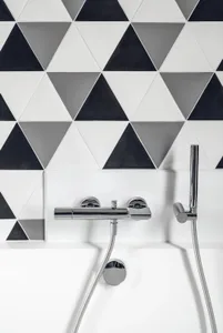 Modern minimalist bathroom with black, white, and gray geometric triangle ceramic tiles, featuring a chrome faucet and hand s