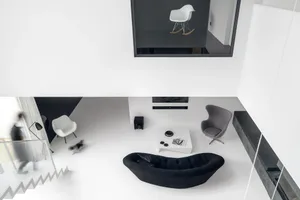 A minimalist living room with concrete flooring, a black sofa, a white coffee table, and a gray armchair.