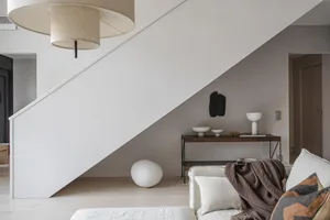 A modern minimalistic living room with neutral tones, showcasing a white sofa, a wooden console table, and a combination of g