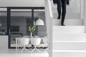 Modern minimalist staircase with concrete steps and a dining area with white chairs and a geometric pendant light.