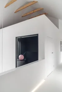 A white minimalist interior with a large window and wooden beams on the ceiling.