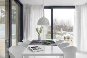 A modern dining area with white chairs, a white table, and a white vase with flowers.