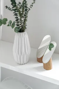 A white ceramic vase with green plant on a white shelf.