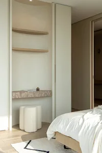 Modern minimalist bedroom with a white marble floating shelf, natural fiber stool, and white bedding.