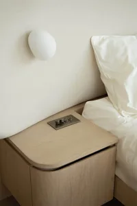 Minimalist bedroom featuring a wooden bedside table with a brushed metal switch panel.