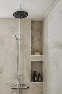 A modern bathroom with concrete tiles, a shower head, and built-in shelves for toiletries.