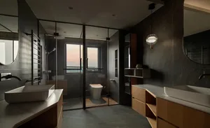 Modern bathroom interior with dark stone walls and floor, dark wood vanity, and clear glass shower enclosure