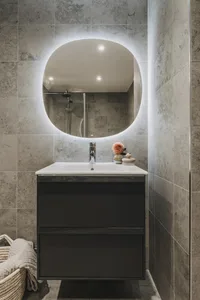A minimalist bathroom with a modern industrial design featuring concrete tiles and a circular mirror with LED lighting.