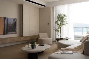 A modern residential interior featuring a neutral color palette, including a sofa, armchair, coffee tables, and a TV cabinet.