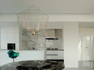Modern kitchen featuring white marble countertops and backsplash with black marble accents, illuminated by a large metallic c