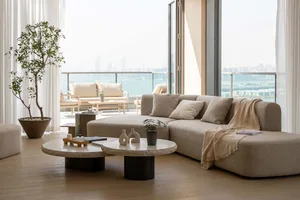 Modern living room with a beige fabric sofa, round coffee tables, a potted plant, and a balcony view.