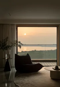 A modern living room with a large glass window showcasing a scenic sunset view.