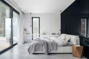 Modern minimalist bedroom featuring concrete flooring, a white leather bed, and wooden nightstand.