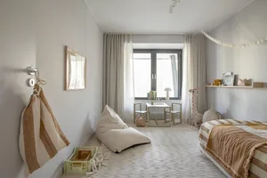 A modern bedroom featuring a bed with striped bedding, a small table and chairs, and a window with curtains.