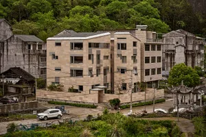 Modern residential building constructed with tan-colored sandstone material, surrounded by greenery and trees.