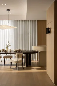 A modern residential interior featuring a wooden dining area with a round table and minimalist furniture, overlooking a citys
