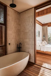 Minimalist bathroom with a concrete bathtub and tiled walls, featuring wooden flooring and accents.