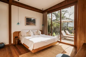 Modern bedroom interior with white floating bed on wooden floors, overlooking a patio with palm trees and lounge chairs.