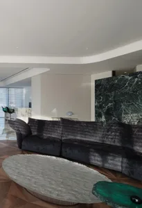 A modern living room featuring a dark velvet couch, a large marble coffee table, and a green marble accent wall.