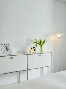 A minimalist bedroom featuring a glass cabinet, white tulips, and a floor lamp.
