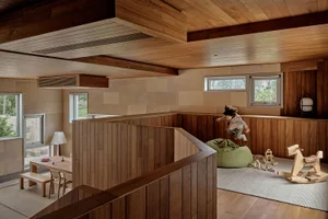 A modern playroom with wooden walls and flooring, featuring a child jumping on a bean bag.