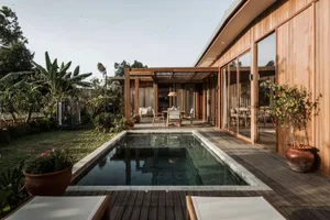 Modern residential patio featuring wooden deck, glass walls, and concrete poolside.