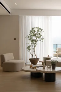 A minimalist living room with textured fabric furniture, a large plant, and round coffee tables.