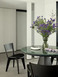 A modern dining room featuring a green marble table with a vase of purple flowers and black chairs.