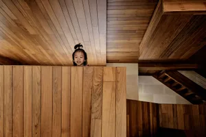 A child plays peek-a-boo behind wooden paneling in a modern interior space.