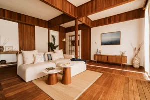 A modern living room featuring a minimalist sofa, coffee tables, and wooden walls and flooring.