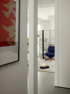 Modern minimalist living room featuring a blue upholstered chair, a small black fireplace, and white walls and floors.