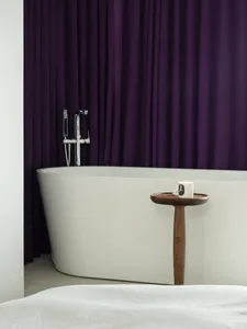 Modern minimalist bathroom featuring a white tub with purple curtains and marble accents.