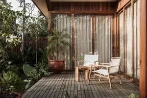 A modern outdoor patio with wooden furniture, plants, and large windows.