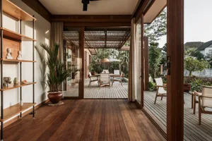 A cozy, open-concept patio area with wooden flooring and furniture, surrounded by lush greenery and natural light.