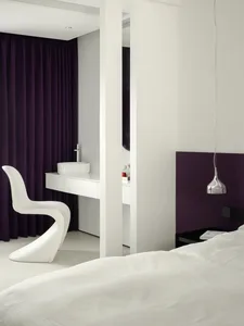 A modern bedroom with white wood flooring, purple accents, and a sleek, white chair.