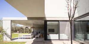 A modern residential exterior featuring a concrete structure with large glass windows and a dog standing on the porch.