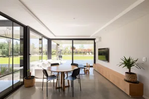 A modern living room with concrete and glass surfaces, a wooden dining table, and black chairs.