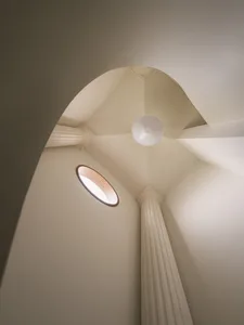 A modern architectural interior featuring a plaster ceiling with a circular window and lamp, along with decorative columns.