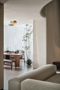 The minimalist living room features a concrete floor and sofa, along with a dining area with a wooden table and chairs.