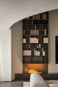 Modern minimalist living room featuring a built-in wooden shelving unit with white and beige books and decorative items.