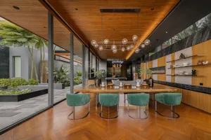 Modern dining room with wooden flooring, chairs, and ceiling, featuring a hanging light fixture and greenery in the backgroun