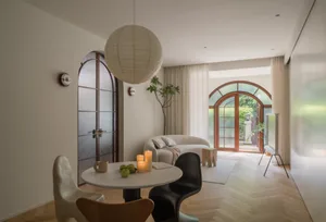 A modern living room with wooden furniture, floor-to-ceiling curtains, and an arched window.
