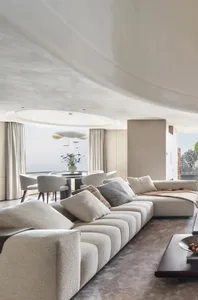 Modern living room featuring a fabric sofa with pillows and a dining area in the background